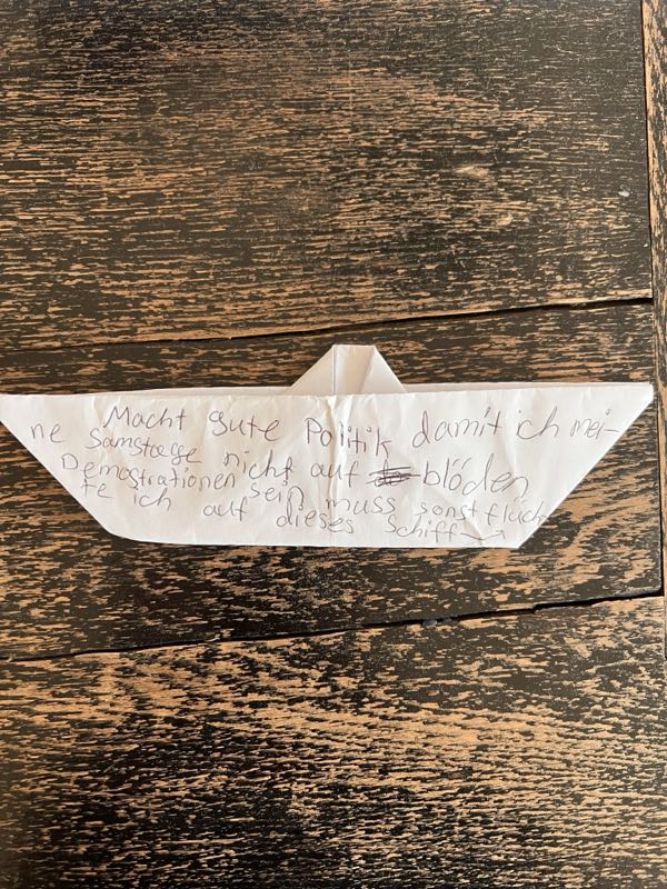 Ein aus einem beschriebenen Zettel gefaltetes Papierschiff auf dunklem Holz